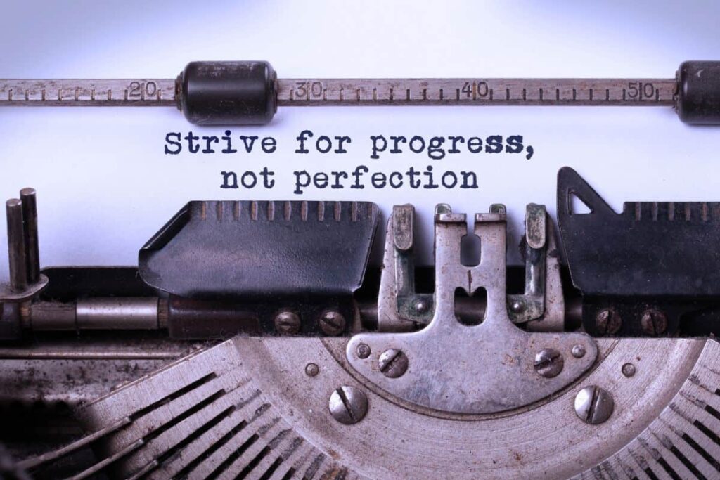 "Strive for progress, not perfection" typed on paper in an old typewriter