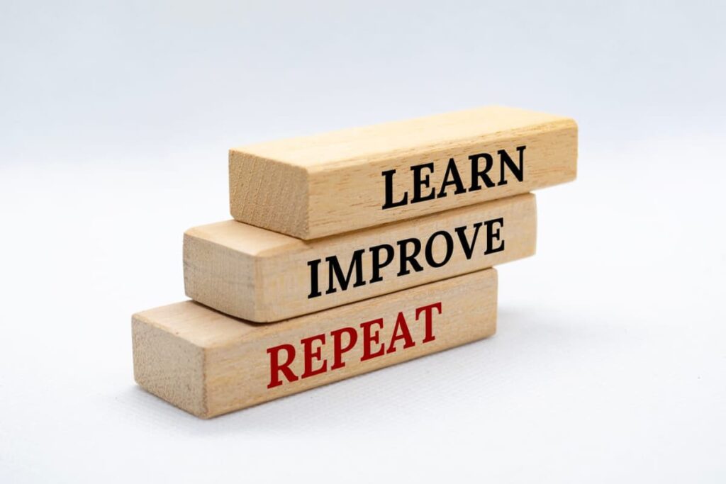 Three wooden blocks stacked like stairs with words on each: "LEARN," "IMPROVE," "REPEAT."