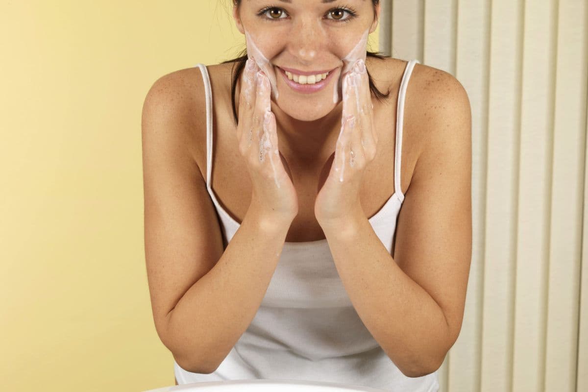 smiling woman washing her face at sink