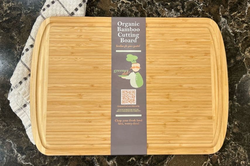 Organic bamboo cutting board on counter with towel in background.
