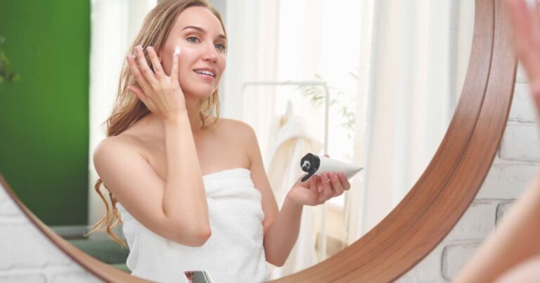 woman looking in mirror and applying skincare