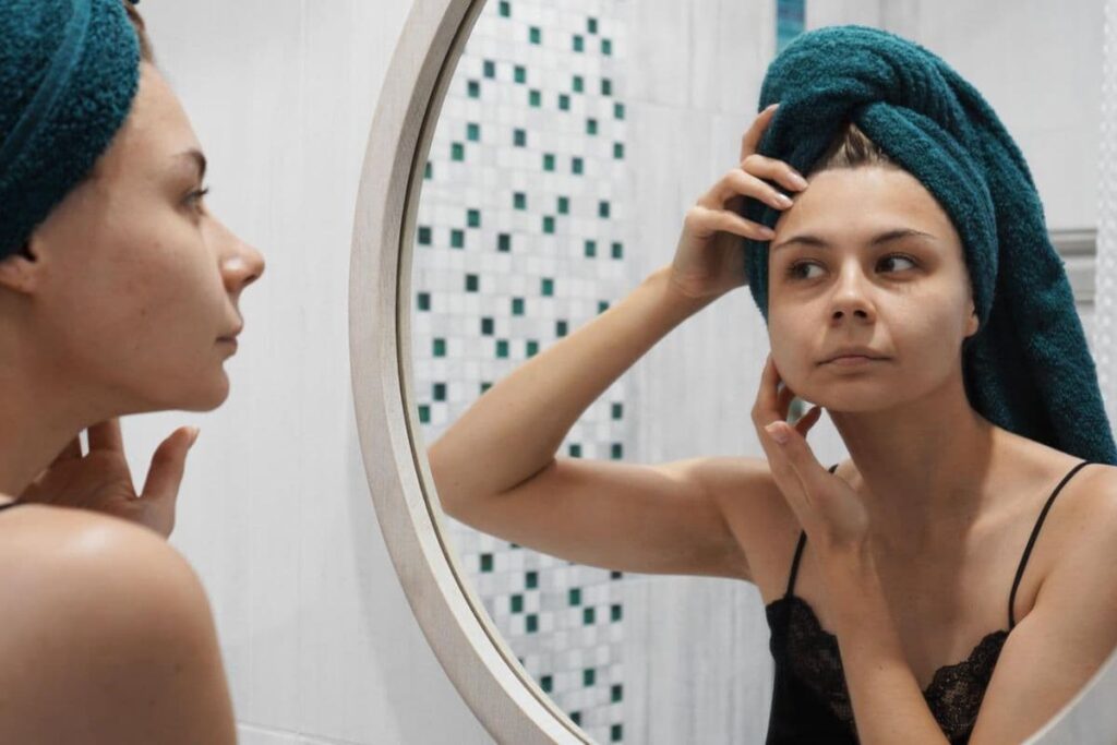 Woman picking her skin at bathroom mirror