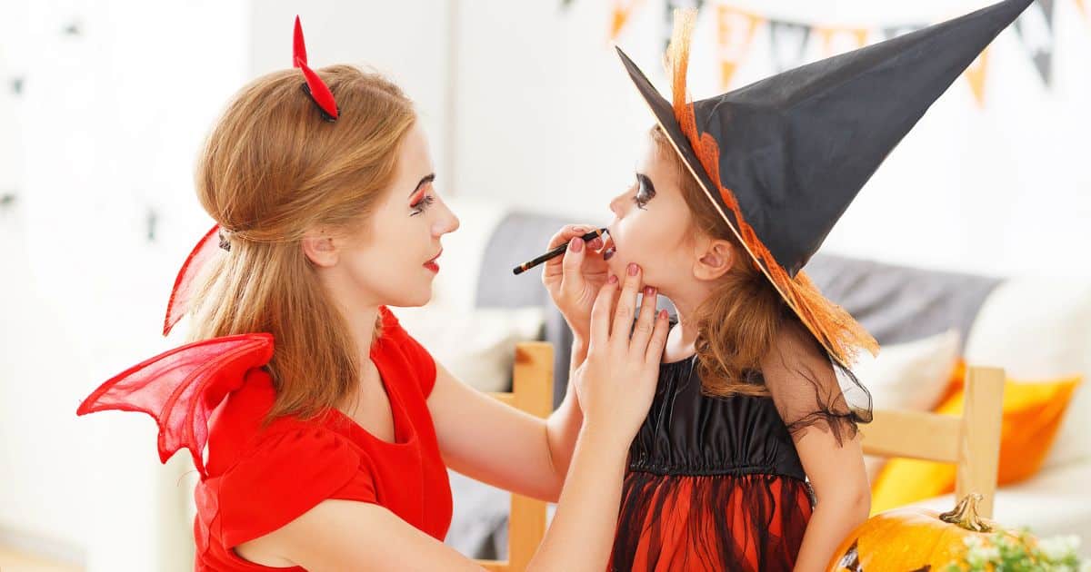 mother and daughter dressed up for Halloween, mother applying makeup to daughter's face