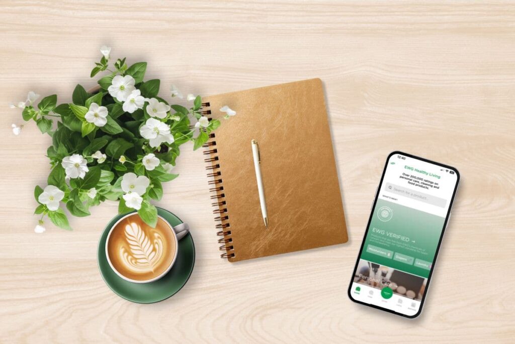 Cup of coffee, notebook, plant, and mobile phone with EWG app open on tabletop.