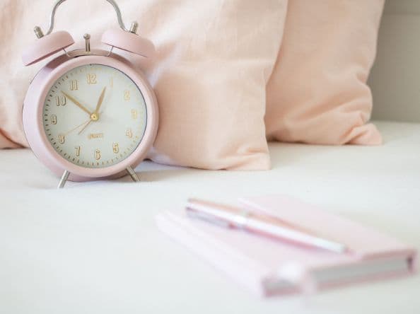 Pink pillows, alarm clock, and journal and pen.