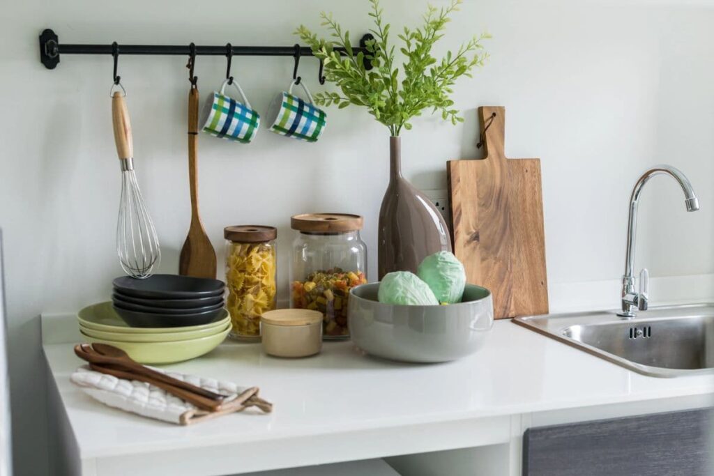Kitchen counter with wooden cooking utensils and cutting board, ceramic bowl and mugs, and glass containers with dry goods.
