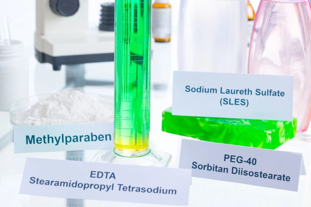 Beakers and bottles labeled with harmful ingredients commonly found in beauty products.