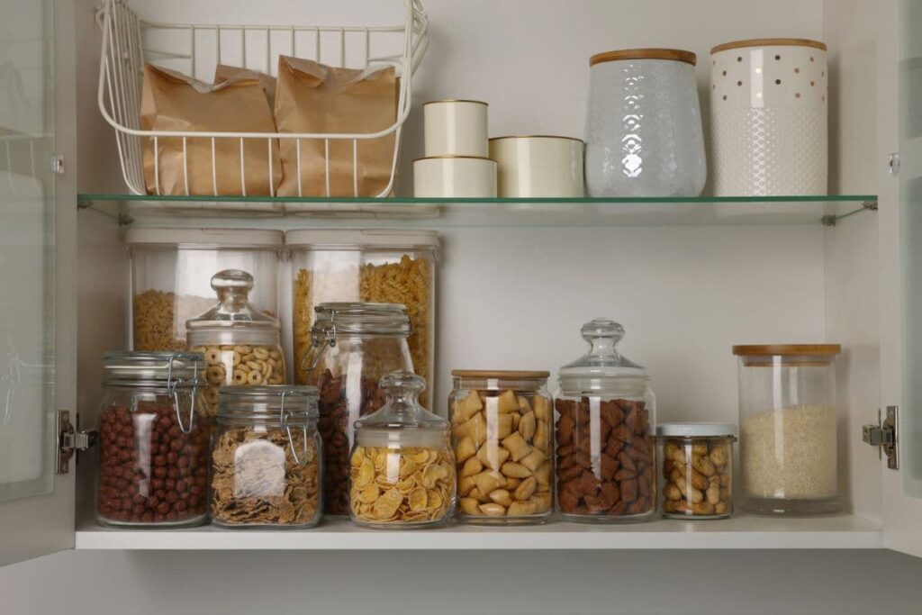 Glass and ceramic jars with dry goods on cabinet shelf.