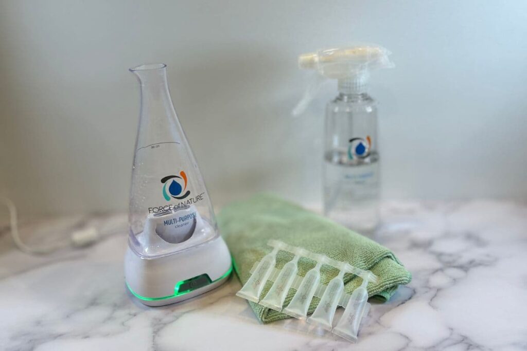 Force of Nature non-toxic cleaning system and solution capsules displayed on counter near a green towel.