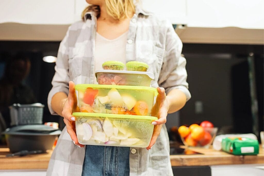Woman holding a stack of plastic storage containers filled with food.