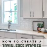 Bright kitchen with white cabinets, a sink below a window, and a framed succulent. Text reads "How to Create a Toxin-Free Kitchen: Your Essential Guide."