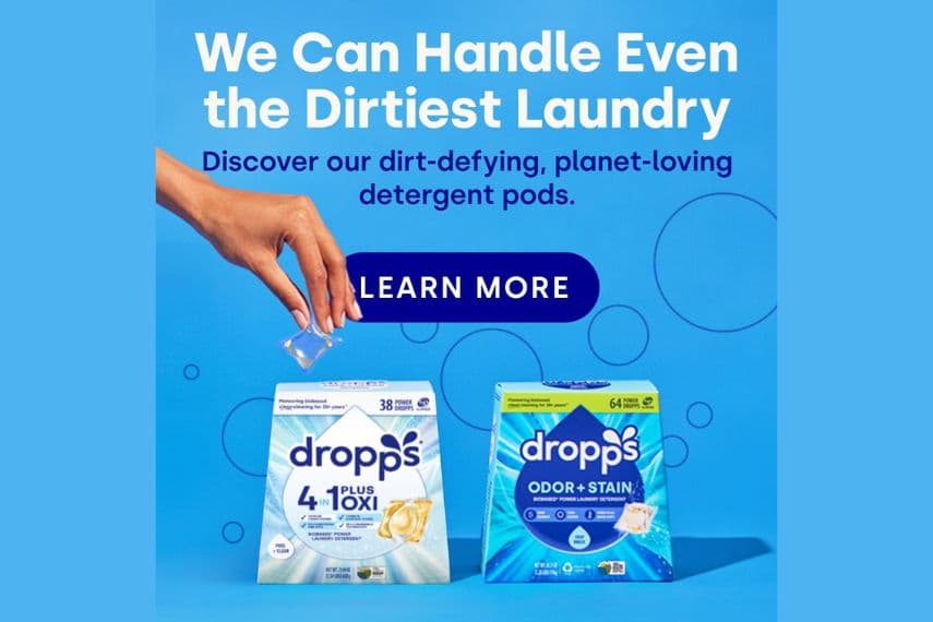 Hand holding a laundry pod above 2 boxes of Dropps laundry detergent.