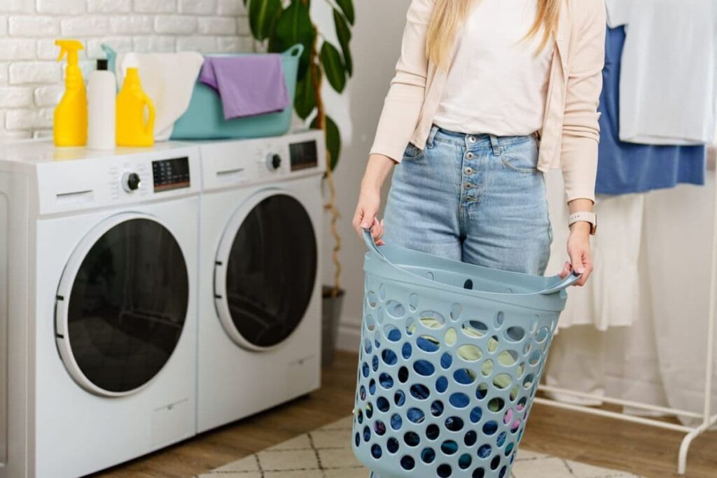 Woman holding laundry basket in front of washer and dryer with safer cleaners.