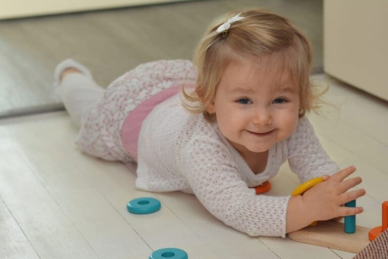 Smiling baby playing with plastic toys on a vinyl floor, illustrating some hidden phthalates in everyday products.