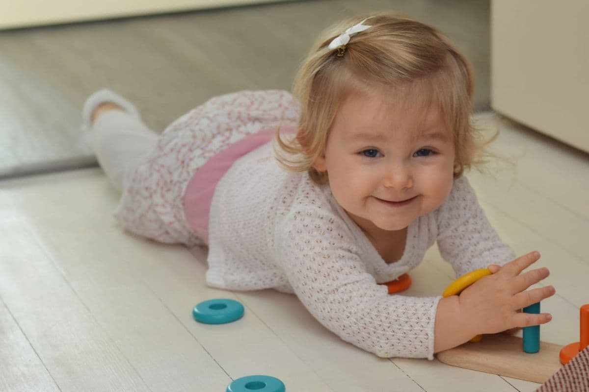 Smiling baby playing with plastic toys on a vinyl floor, illustrating some hidden phthalates in everyday products.