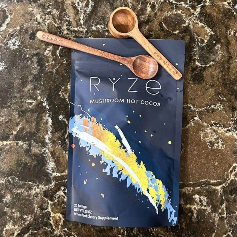 Ryze mushroom hot cocoa, wooden spoon and wooden measuring spoon on counter.