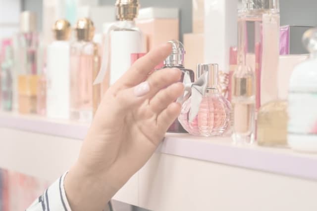 Hand reaching for bottle of fragrance on shelf.