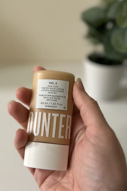Counter Dew Skin Tinted SPF mineral sunscreen on table with plant out of focus in background