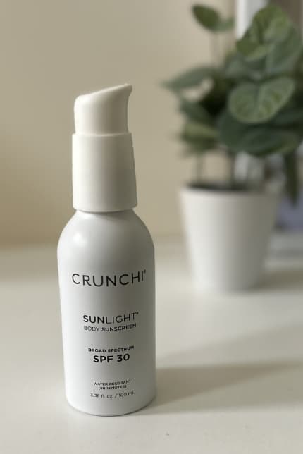 Crunchi Sunlight Body mineral sunscreen on table with plant out of focus in background