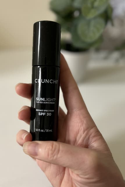 Crunchi Tinted SPF mineral sunscreen on table with plant out of focus in background