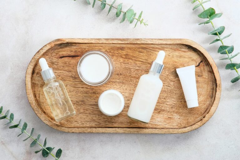 Clean beauty skincare products on a wooden tray with dropper bottles, cream jar, and eucalyptus leaves
