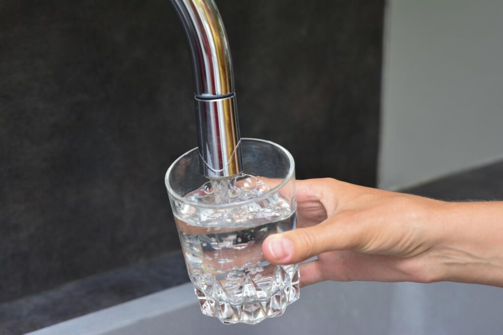 A hand holds a clear glass under a kitchen faucet, filling it with water. Conveys the importance of what's in your water.