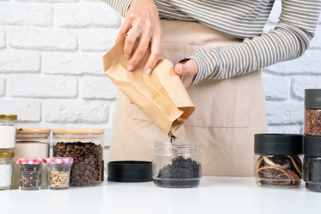 Person pouring tea from a brown paper bag into a jar. Other repurposed glass jars are on the counter.