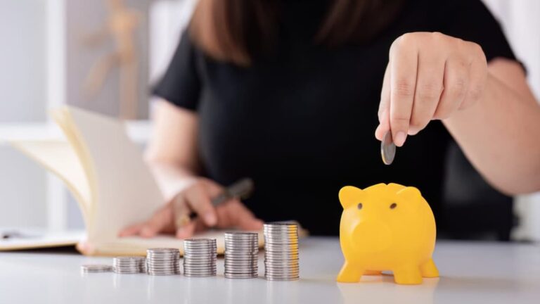 Woman's hand putting coins in a piggy bank for saving money concept.